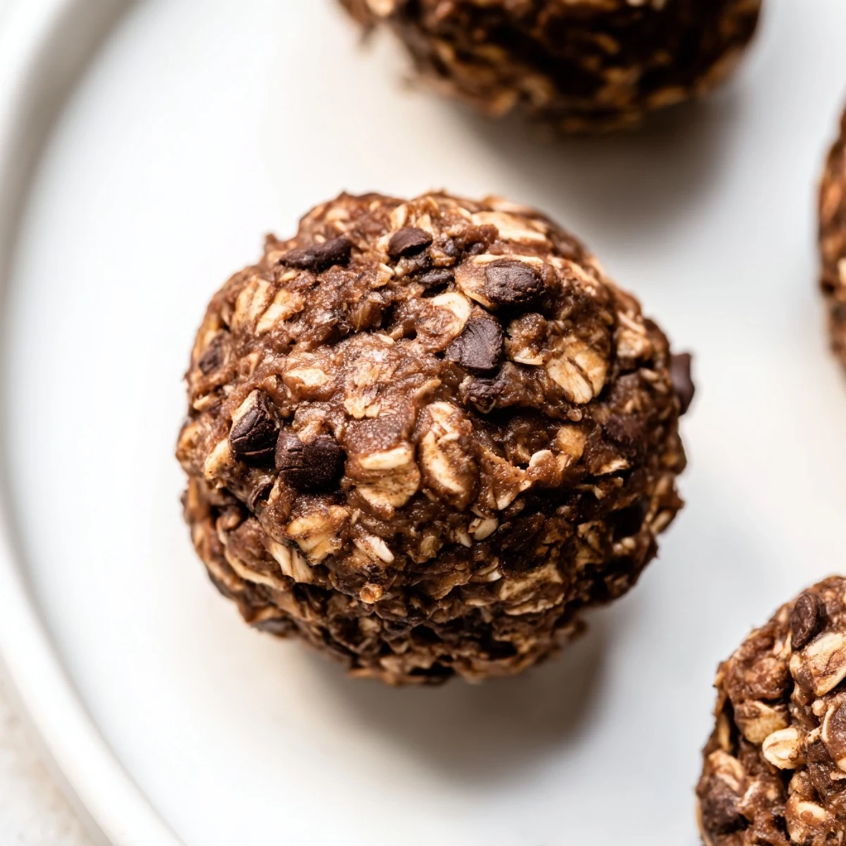 A close-up of Chocolate Peanut Butter Energy Balls on a rustic wooden board, showing oats and chocolate chips. 