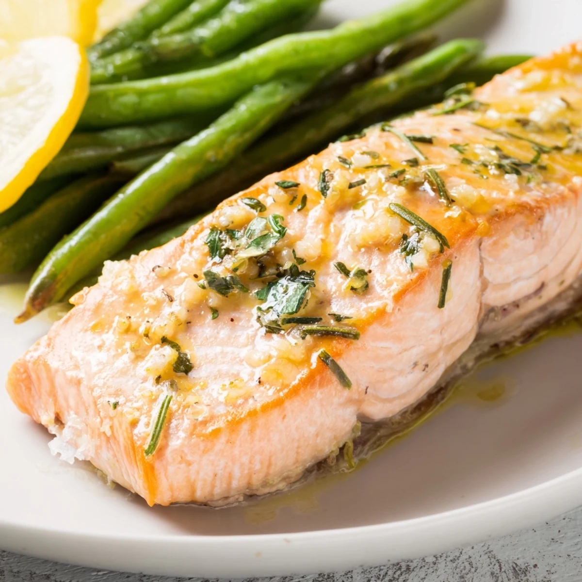 Golden-baked Sheet Pan Salmon and Green Beans with Lemon glistens with olive oil and fresh thyme on a dark sheet pan.