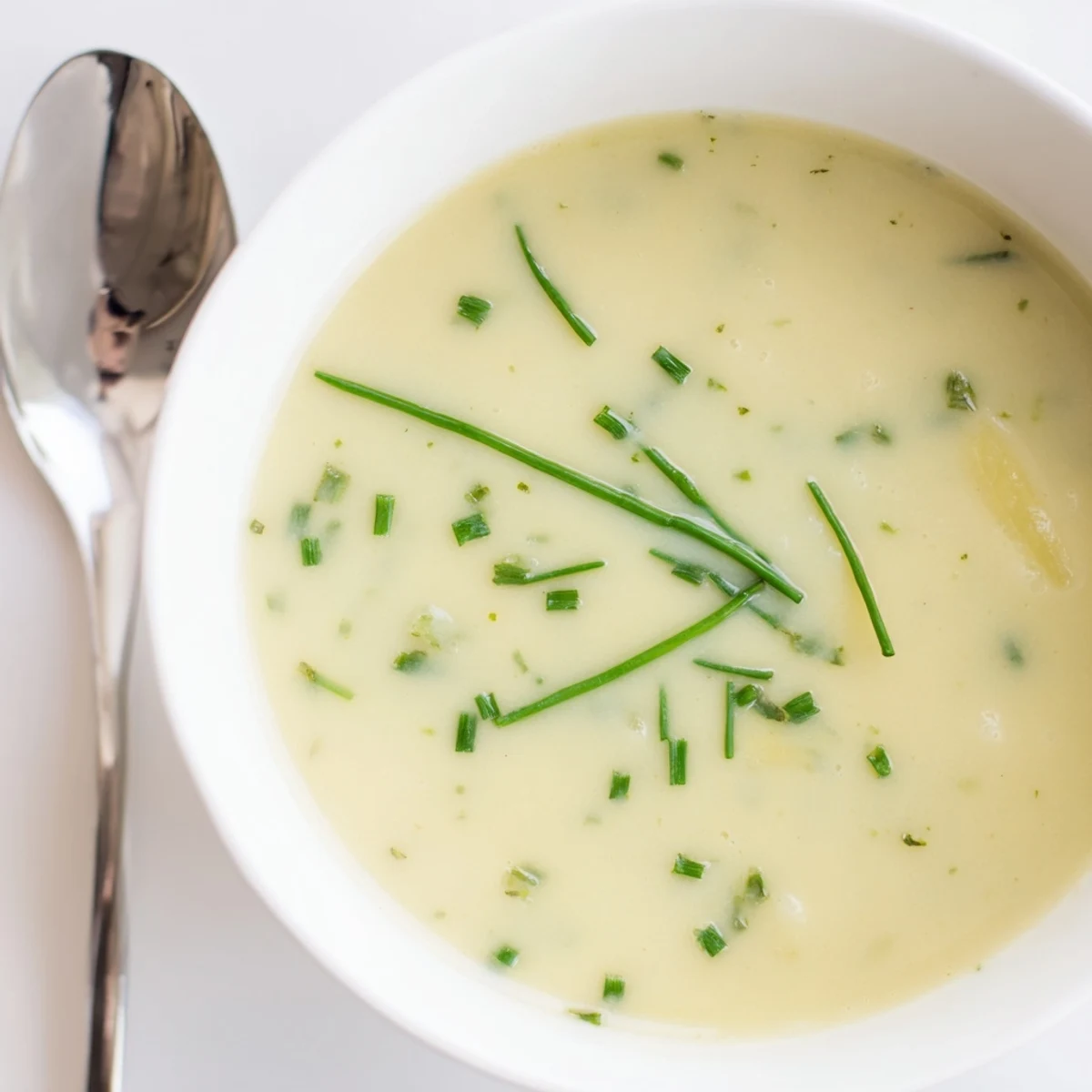 Creamy potato leek soup with chives garnish in a rustic bowl on a wooden table.