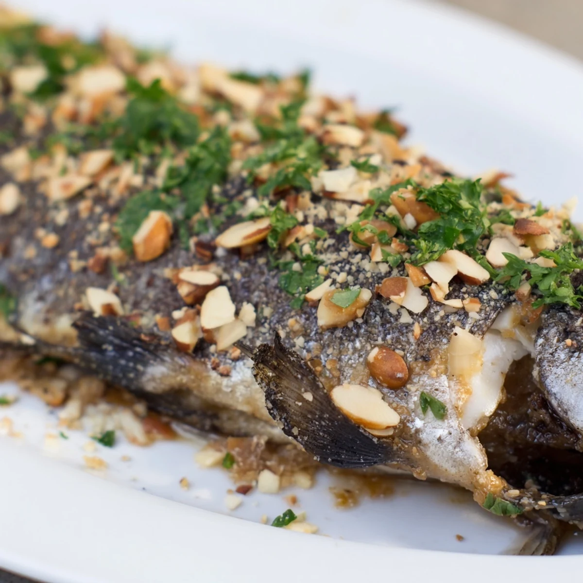 Four servings of baked trout with almond butter, garnished with dill and lemon slices on a white plate.
