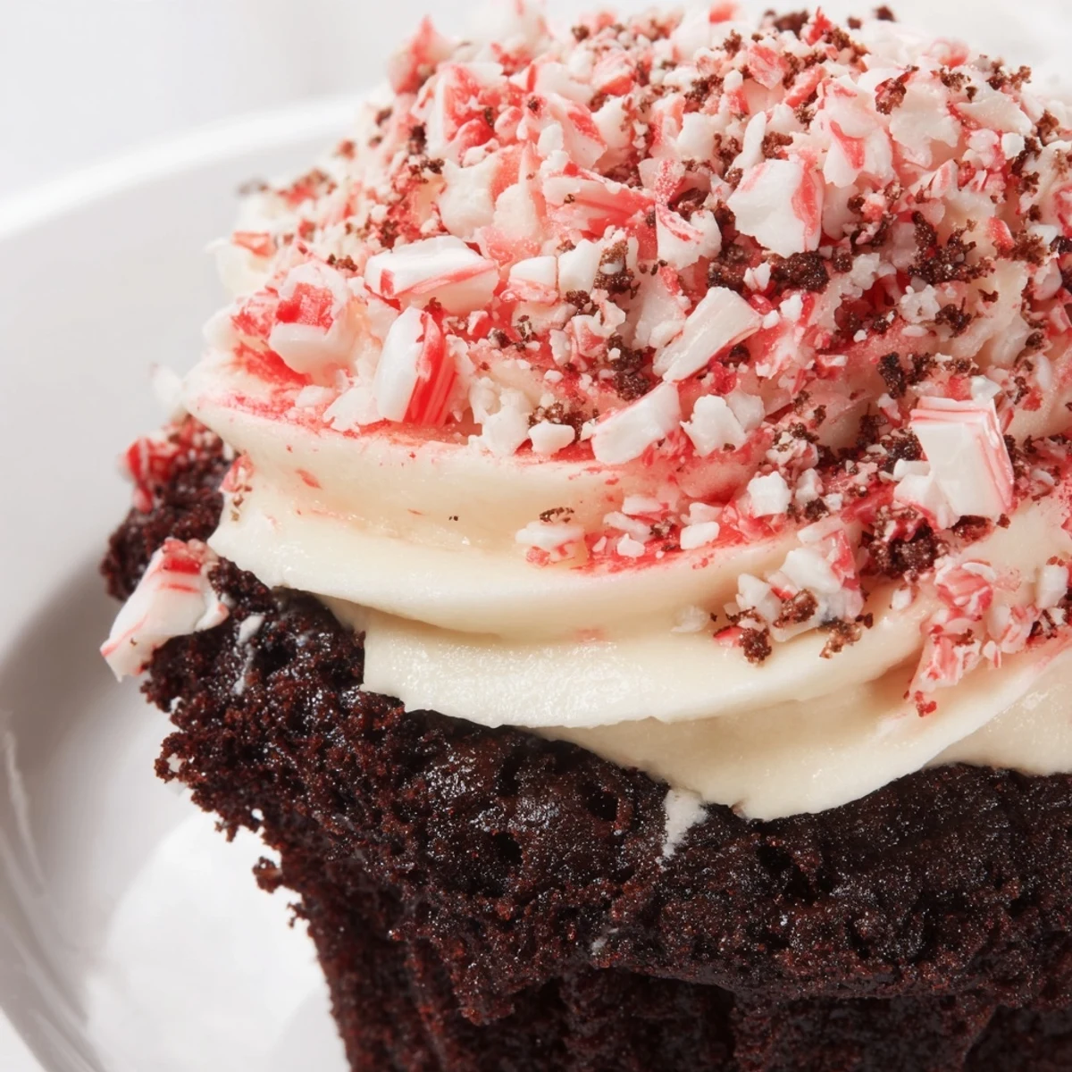 Two moist Chocolate Peppermint Swirl Cupcakes with peppermint buttercream and candy cane pieces paired with a steaming mug of hot cocoa.