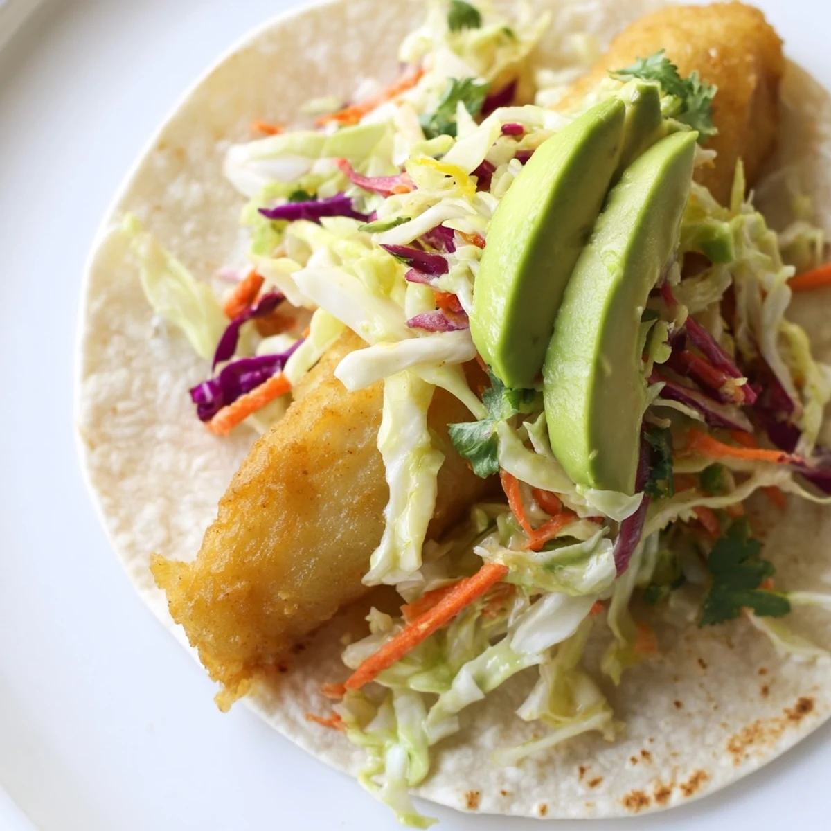 Golden crispy fish fillets nestled in warm corn tortillas with fresh avocado slices and tangy lime wedges on a rustic wooden table.