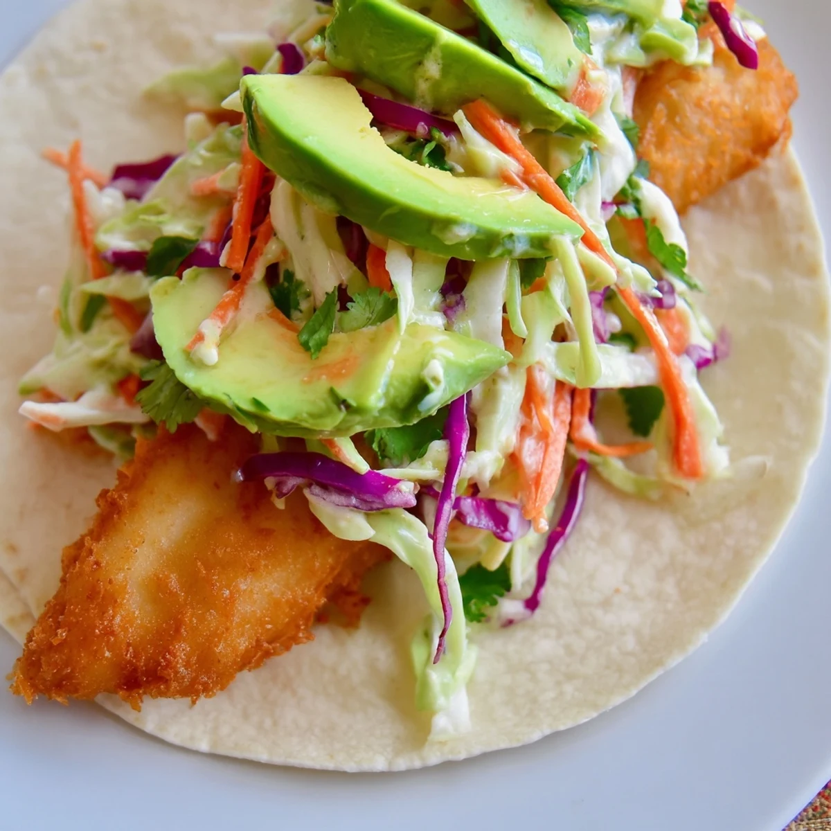 A close-up of crunchy beer-battered fish tacos filled with colorful cabbage slaw and vibrant cilantro, drizzled with creamy avocado sauce.