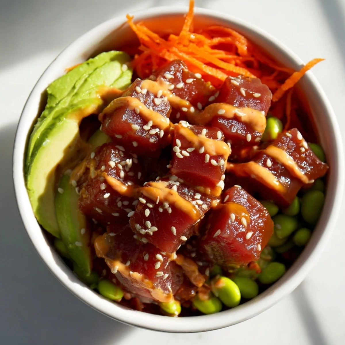 Bright overhead shot of a colorful Spicy Tuna Poke Bowl with Sriracha Mayo, garnished with nori strips, sesame seeds, and green onions, served in a ceramic bowl on a textured table.