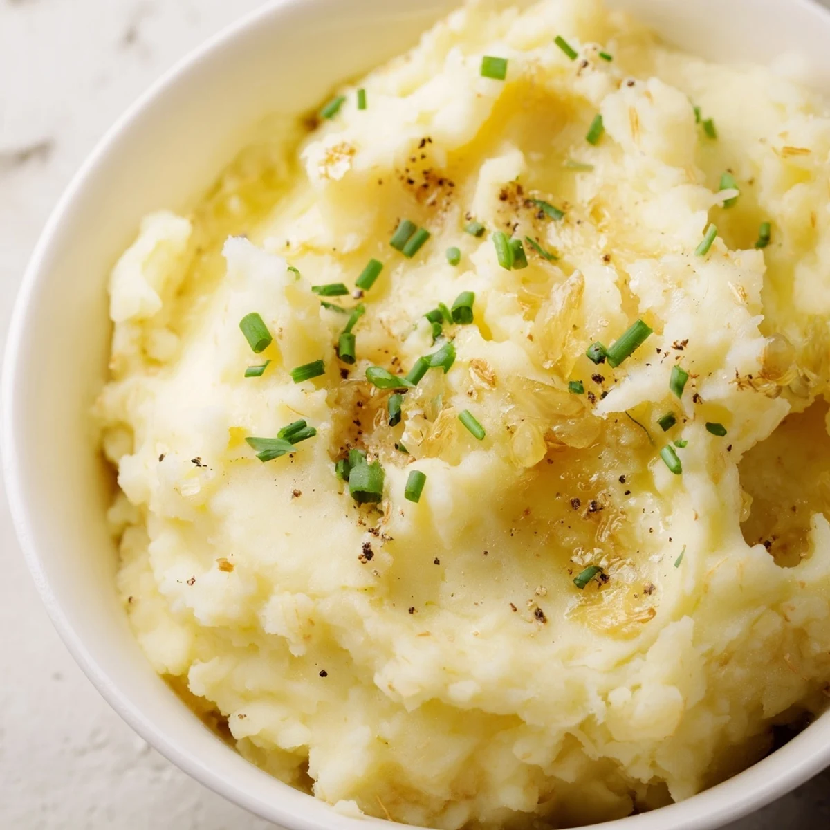 Creamy, velvety Roasted Garlic Mashed Potatoes served warm in a rustic bowl and topped with fresh chives.