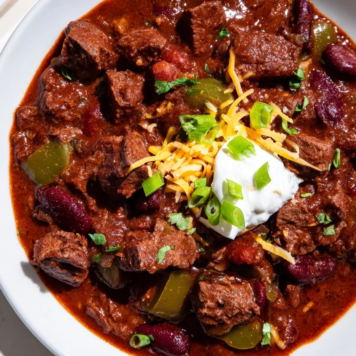 A bowl of Slow Cooker Beef Chili with Kidney Beans and Tomato, steaming and garnished with cheddar cheese and fresh cilantro.