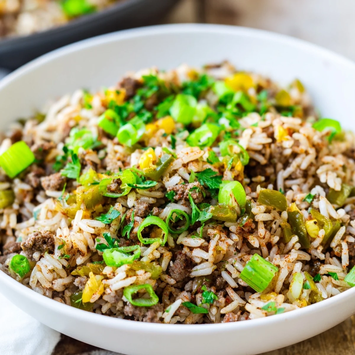 A hearty serving of Mardi Gras Dirty Rice with ground beef is garnished with fresh green onions and parsley, ready to enjoy.