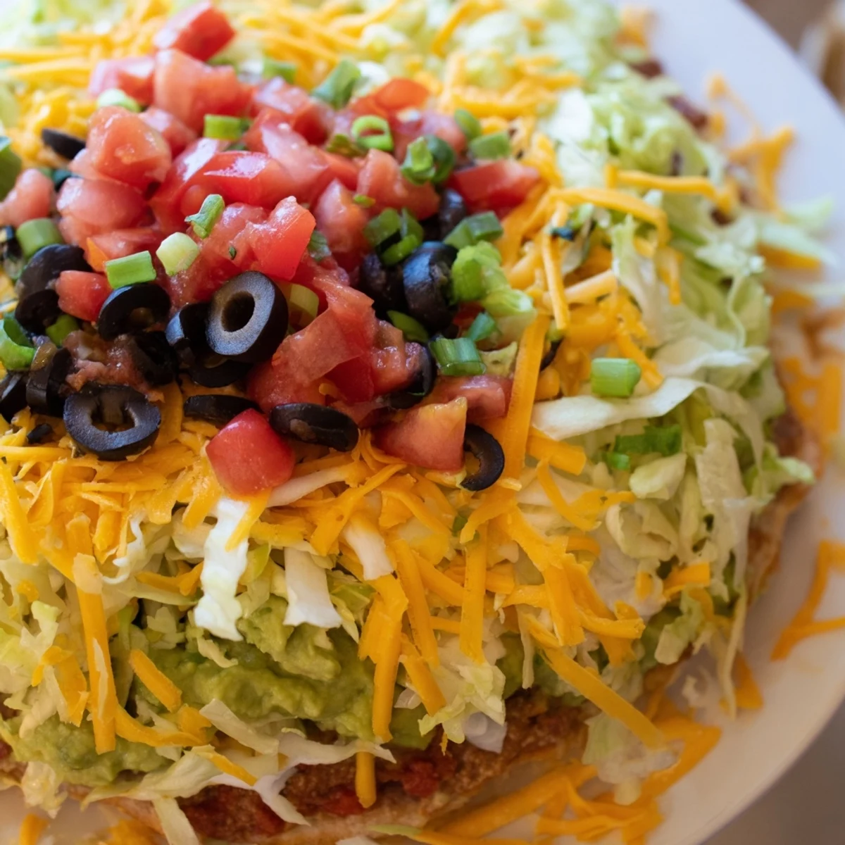 Served in a clear dish, the End Zone Seven Layer Taco Dip shows thick, creamy layers and a scattering of black olives and green onions ready for dipping.