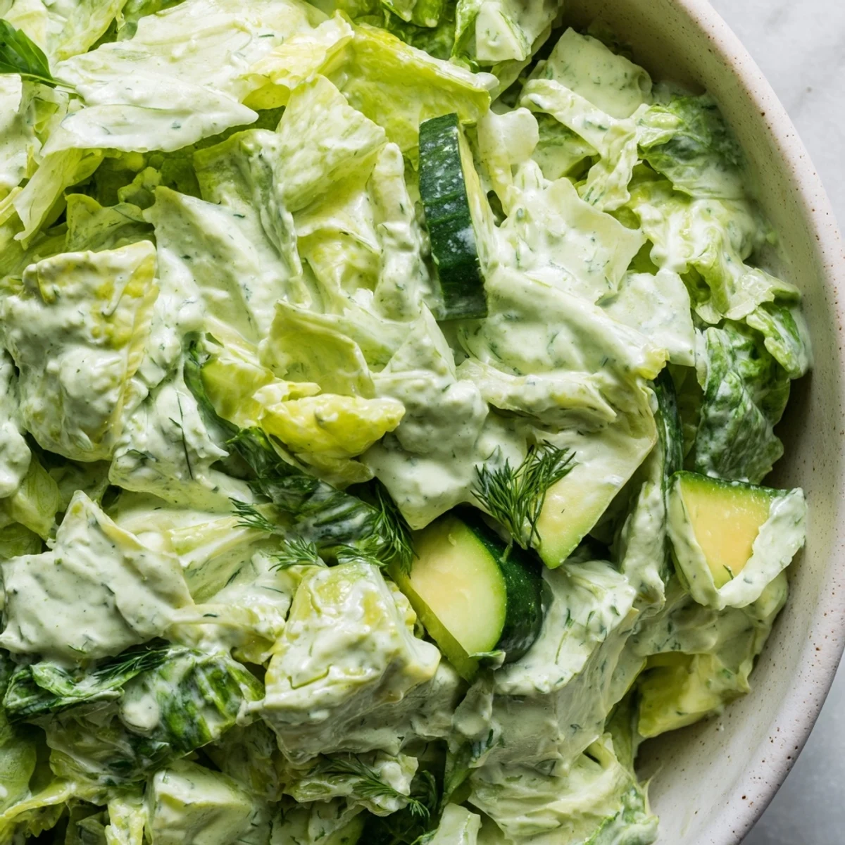 A close-up of the Green Goddess Salad showcasing creamy avocado cubes and crisp chopped vegetables, all tossed in a vibrant green herb dressing.