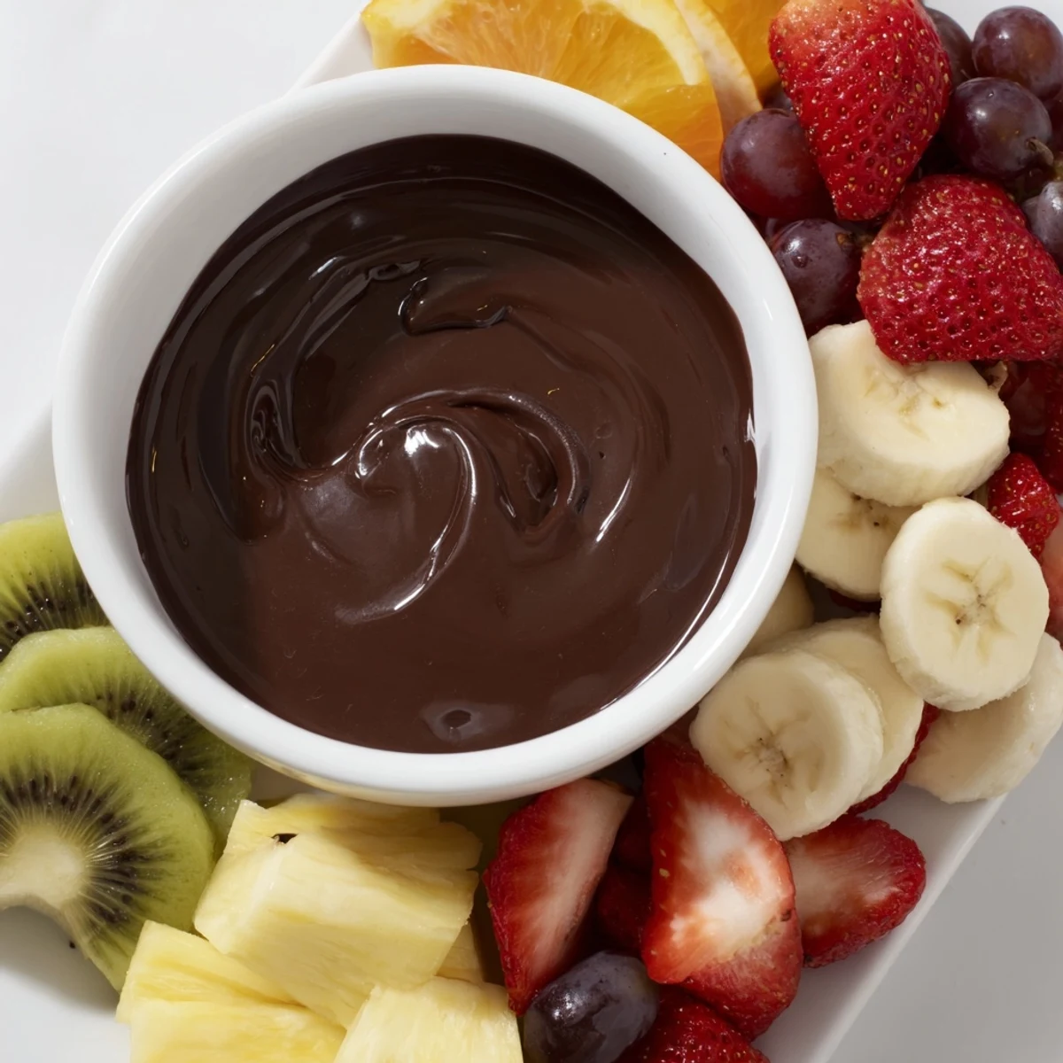 Glossy Romantic Chocolate Fondue with Fruit Platter is surrounded by banana slices, grapes, and cubes of pound cake for dipping.