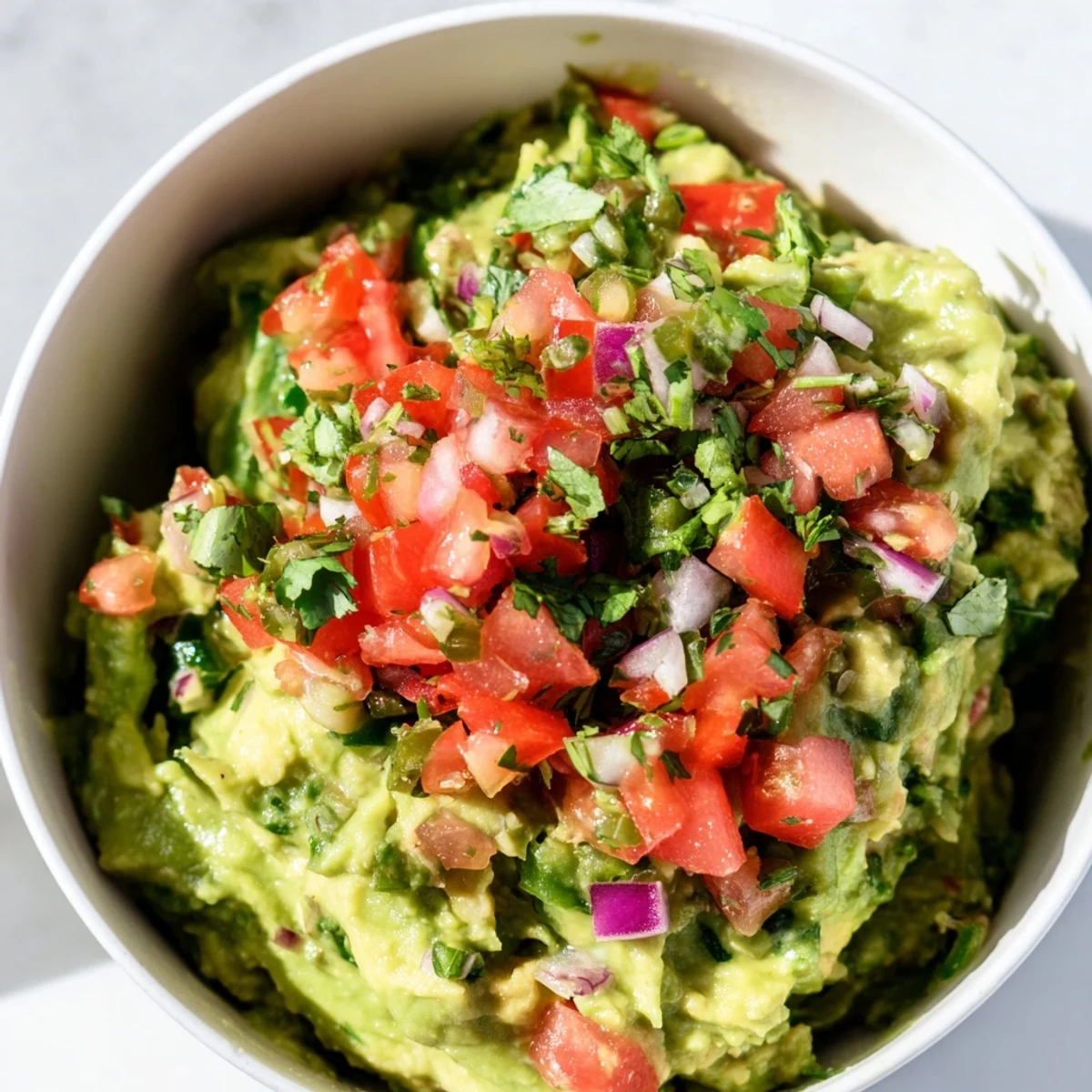 A bowl of homemade guacamole with chunky pico de gallo, topped with fresh cilantro and lime wedges, served with crispy tortilla chips for dipping.