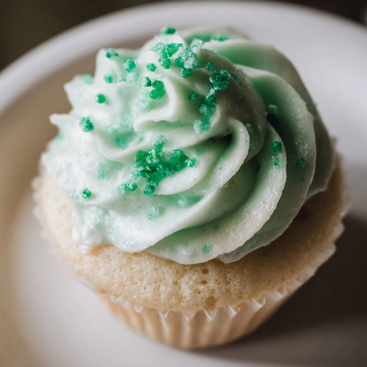 Four fluffy Shamrock Shake Cupcakes topped with creamy mint green frosting and green sprinkles sit on a rustic wooden surface.  