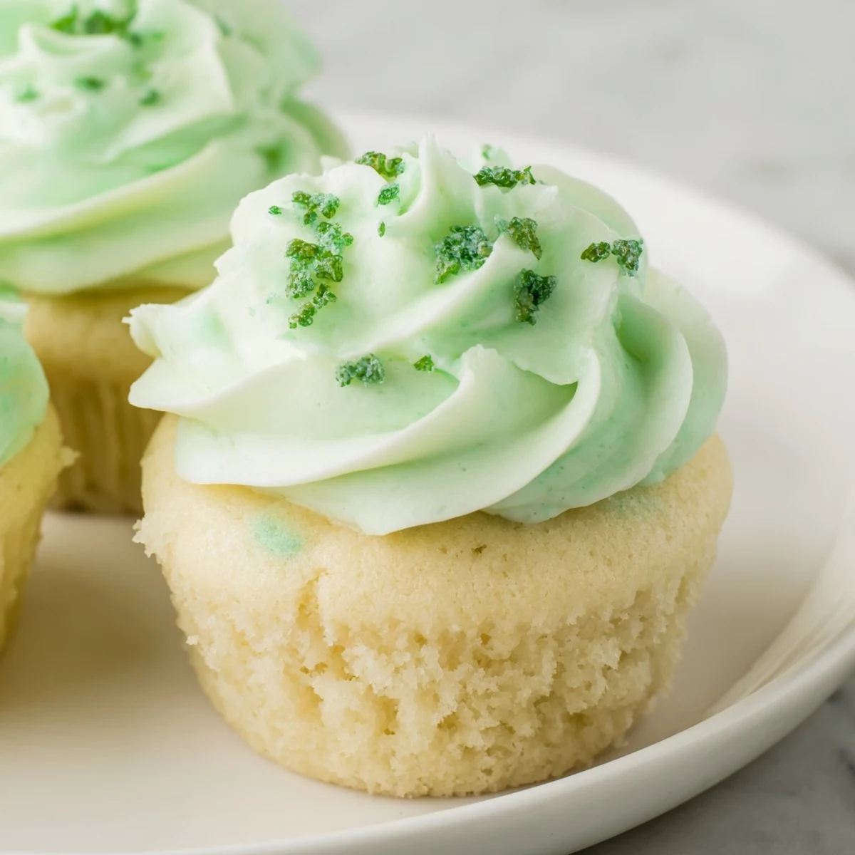 Shamrock Shake Cupcakes arranged on a white plate with fresh mint leaves and a glass of milk for a sweet pairing.