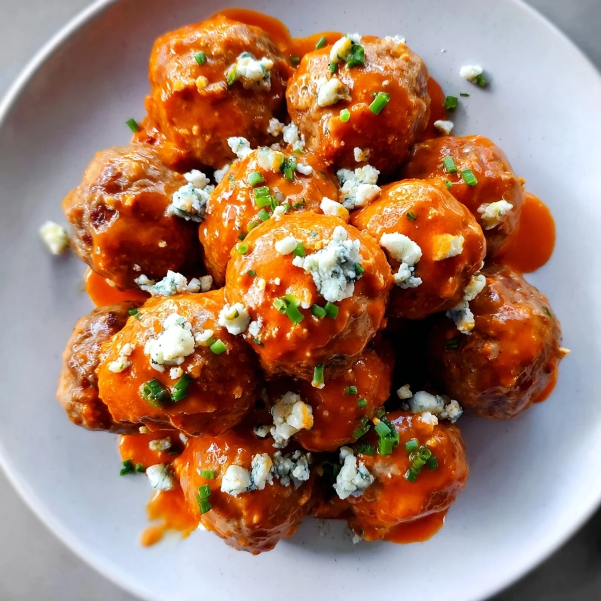 Golden-baked Buffalo chicken meatballs glazed in tangy sauce, topped with crumbled blue cheese and fresh chives on a platter.  