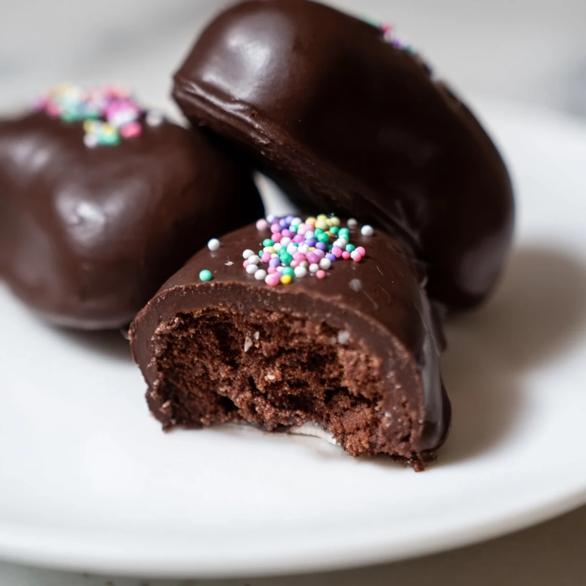 A close-up of homemade Chocolate Covered Marshmallow Peeps on a baking sheet, with glossy chocolate coating and colorful sprinkles adding a festive touch.
