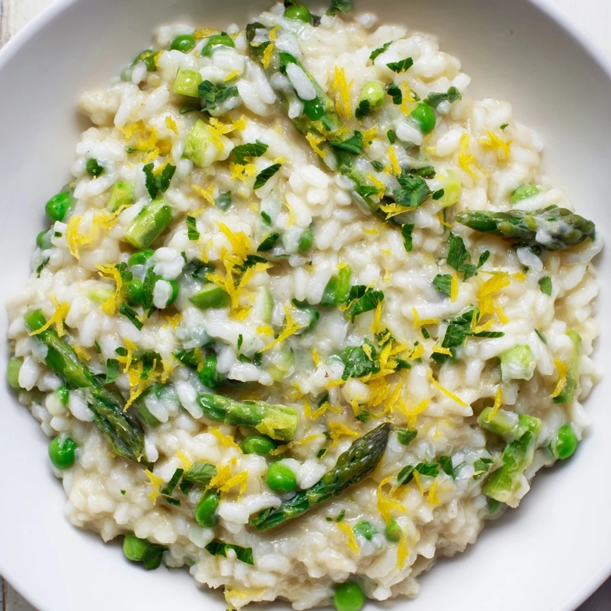 Spring Pea and Asparagus Risotto is served warm on a wooden table with a glass of white wine nearby.
