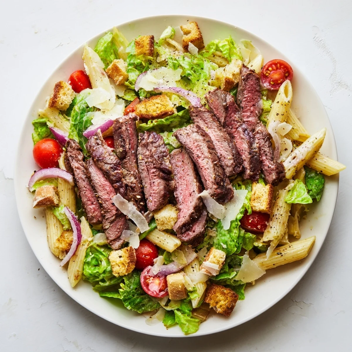 Freshly grilled steak slices rest atop a vibrant bowl of Flavorful Steak Caesar Pasta Salad with crisp romaine and cherry tomatoes.