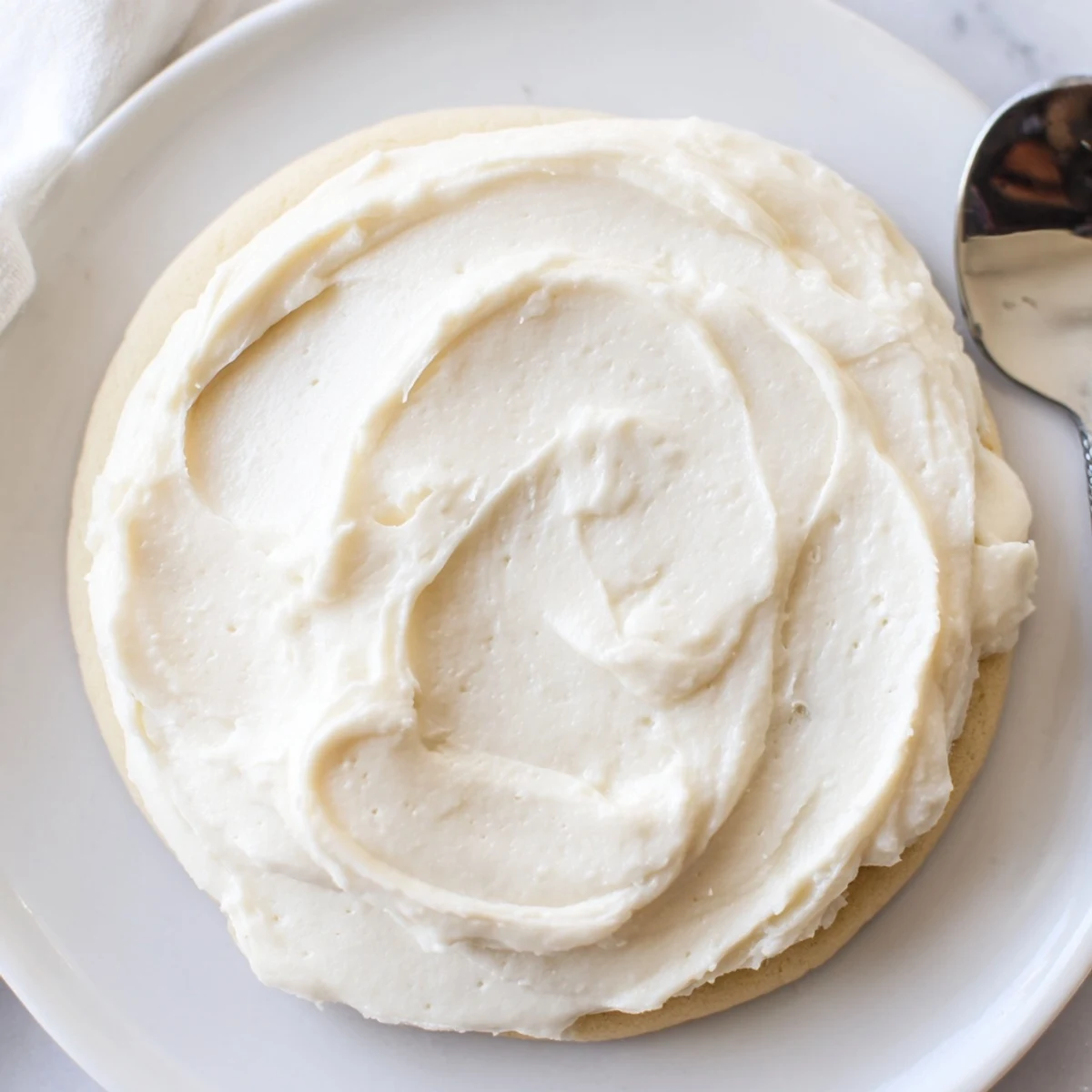Easy Sugar Cookie Frosting in a white bowl, smooth texture perfect for decorating sugar cookies with a knife nearby.