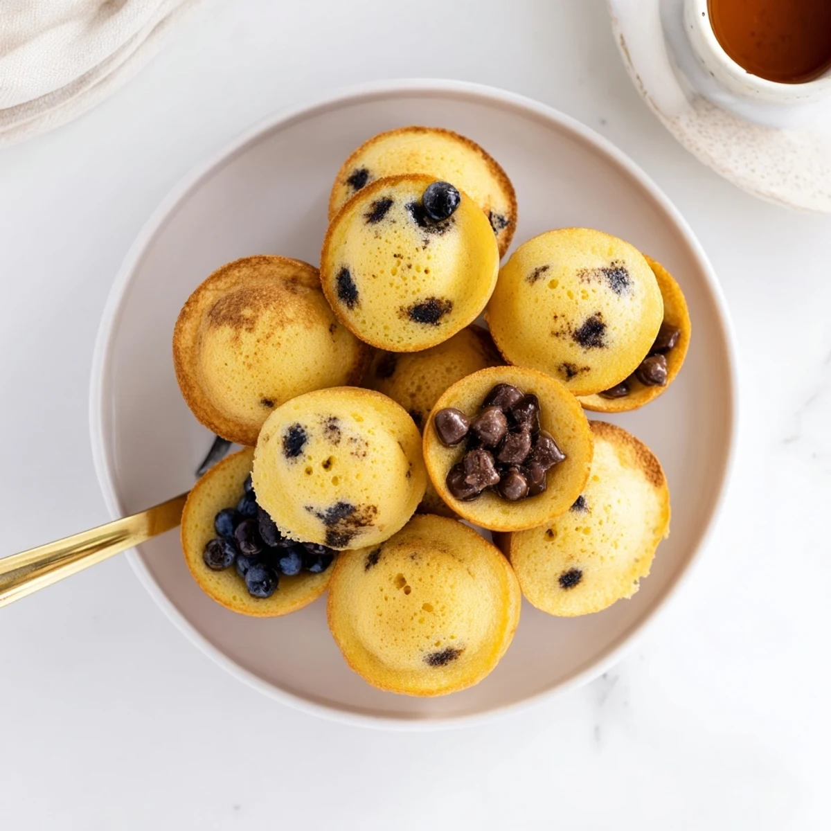 A close-up of fluffy pancake poppers studded with blueberries, served alongside a small bowl of warm syrup for dipping.