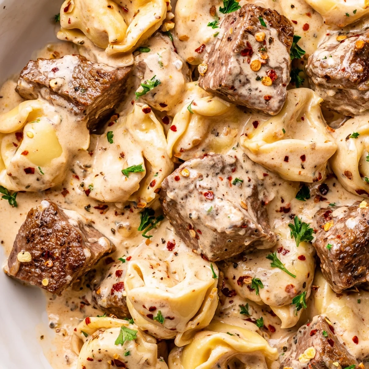 Tender Garlic Steak Tortellini twirled on a fork over a white bowl, garnished with fresh parsley.