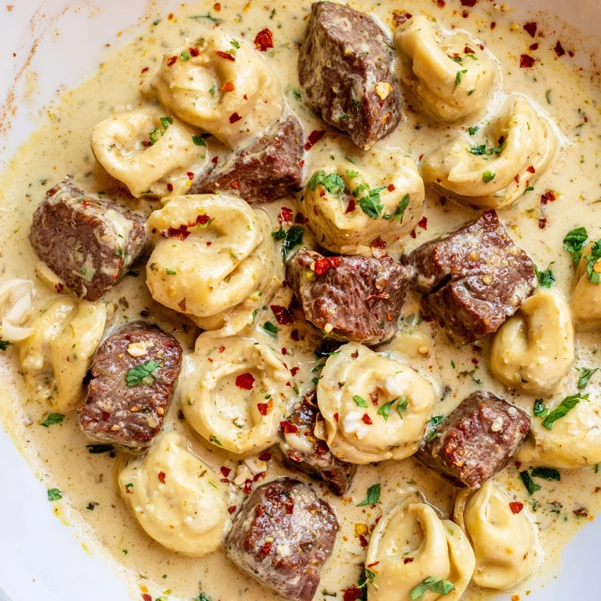 Creamy Garlic Steak Tortellini with seared sirloin cubes and rich parmesan sauce on a rustic dinner plate.
