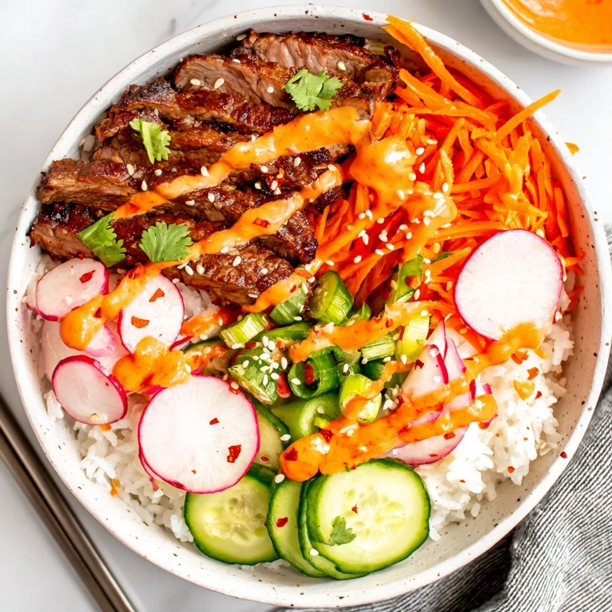Tender beef slices over rice in Korean BBQ Steak Rice Bowls with Spicy Cream Sauce garnished with sesame seeds and spring onions.