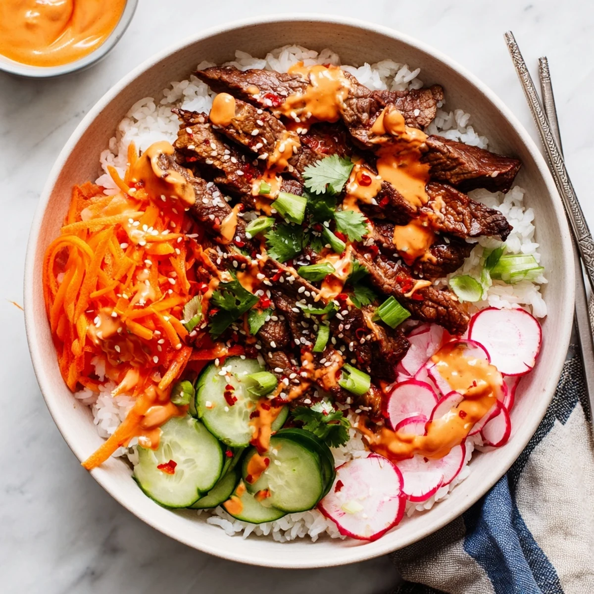 Close-up of Korean BBQ Steak Rice Bowls with Spicy Cream Sauce showcasing juicy steak, shredded carrots, cucumbers, and a spicy mayo-like drizzle.