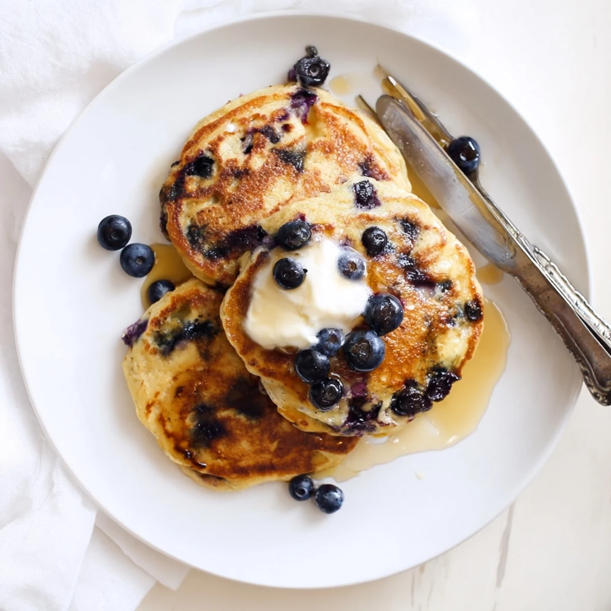 Golden stack of fluffy Greek yogurt blueberry pancakes drizzled with maple syrup and topped with fresh blueberries