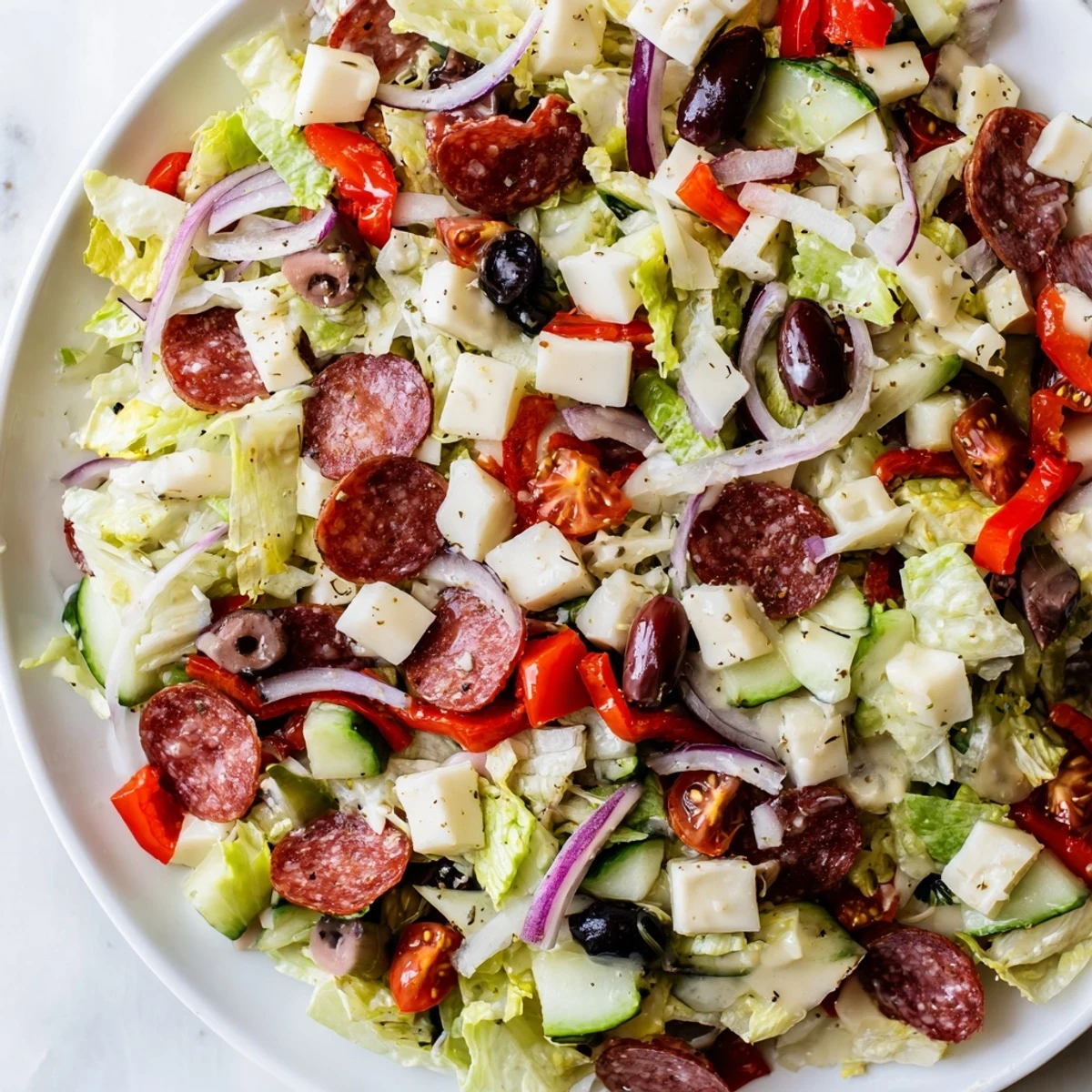 Vibrant bowl of Italian chopped salad featuring crisp romaine, tomatoes, olives, and mozzarella tossed in tangy homemade dressing