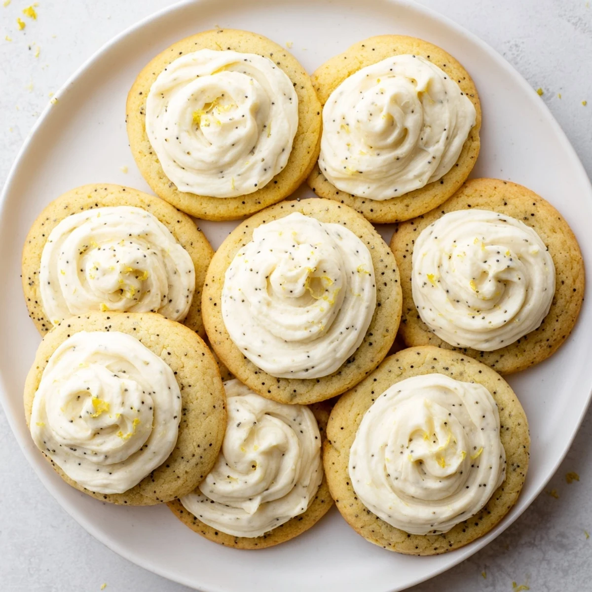 Golden lemon poppy seed cookies topped with swirls of creamy cheesecake frosting on a white plate