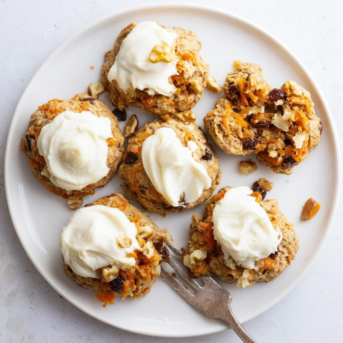 Homemade carrot cake cookies stacked on a white plate with fluffy cream cheese frosting dripping down the sides