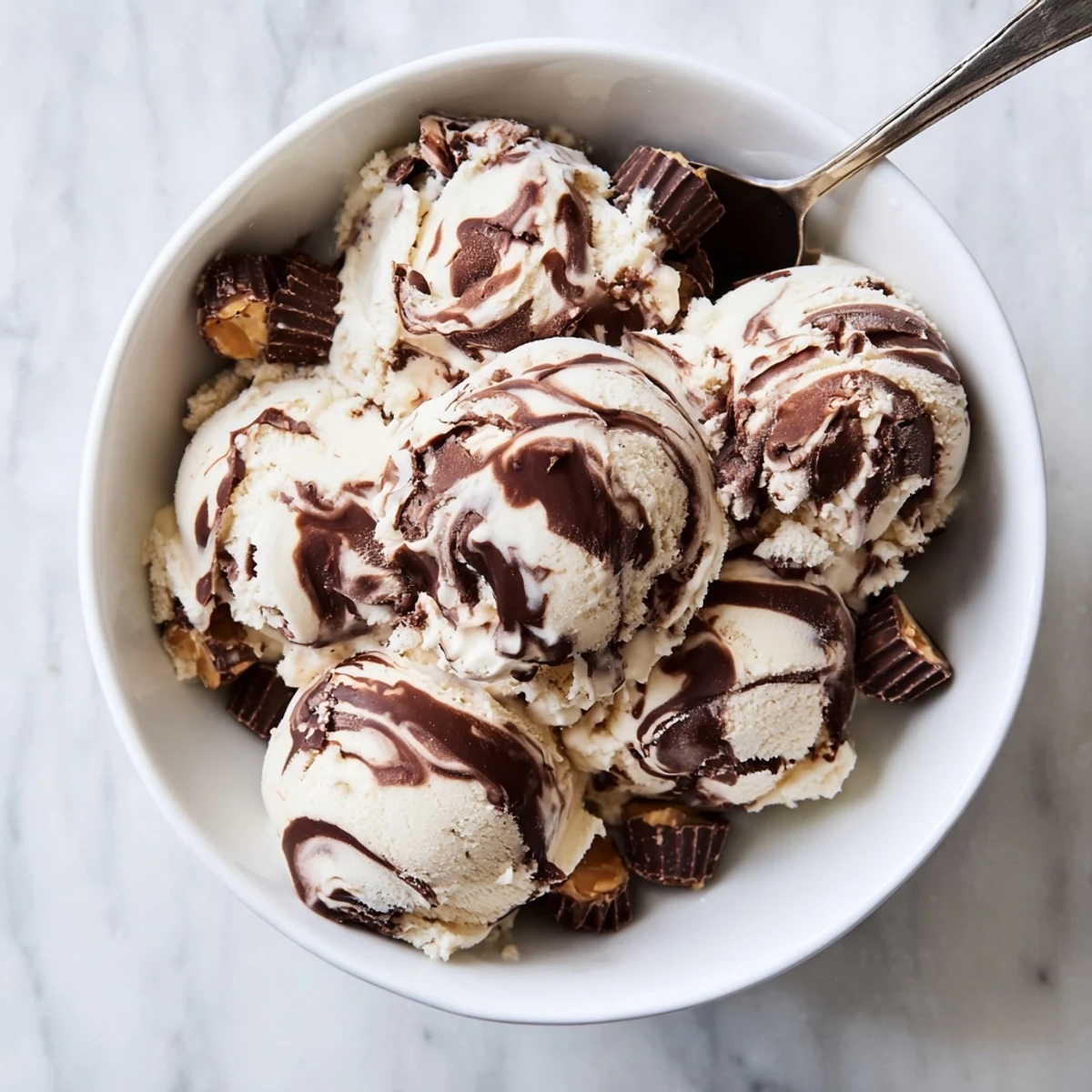 Scoop of velvety moose tracks ice cream topped with fudge ribbons and peanut butter cup pieces on a rustic wooden board