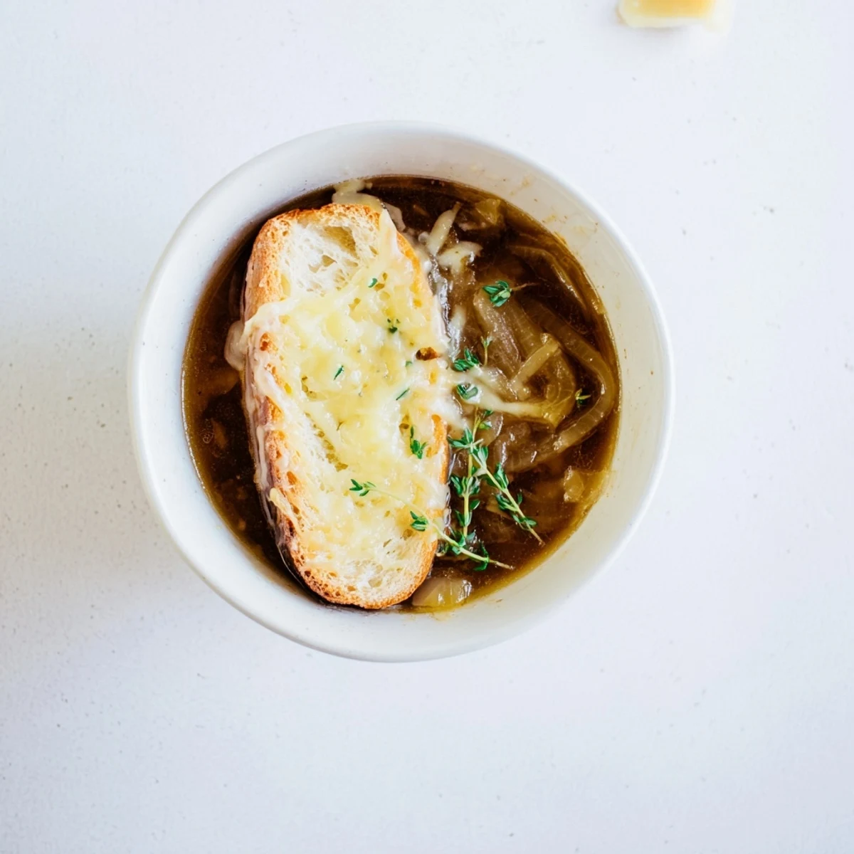 Golden brown caramelized onions float in rich French onion soup beneath bubbly melted Gruyère cheese and crusty toasted bread