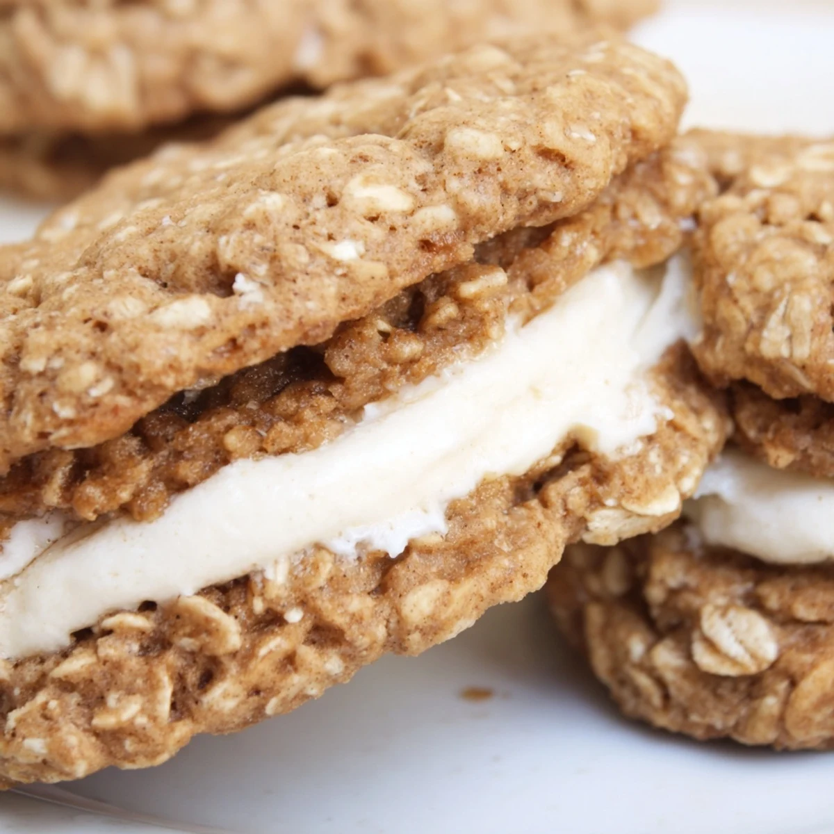 Golden brown oatmeal cookies stacked with fluffy white cream filling creating classic homemade oatmeal cream pies