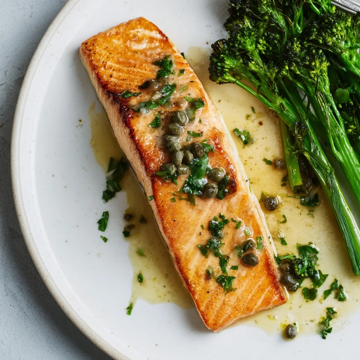 Restaurant-style Gordon Ramsay pan fried salmon fillets served with tender broccoli and lemon wedges on white plate