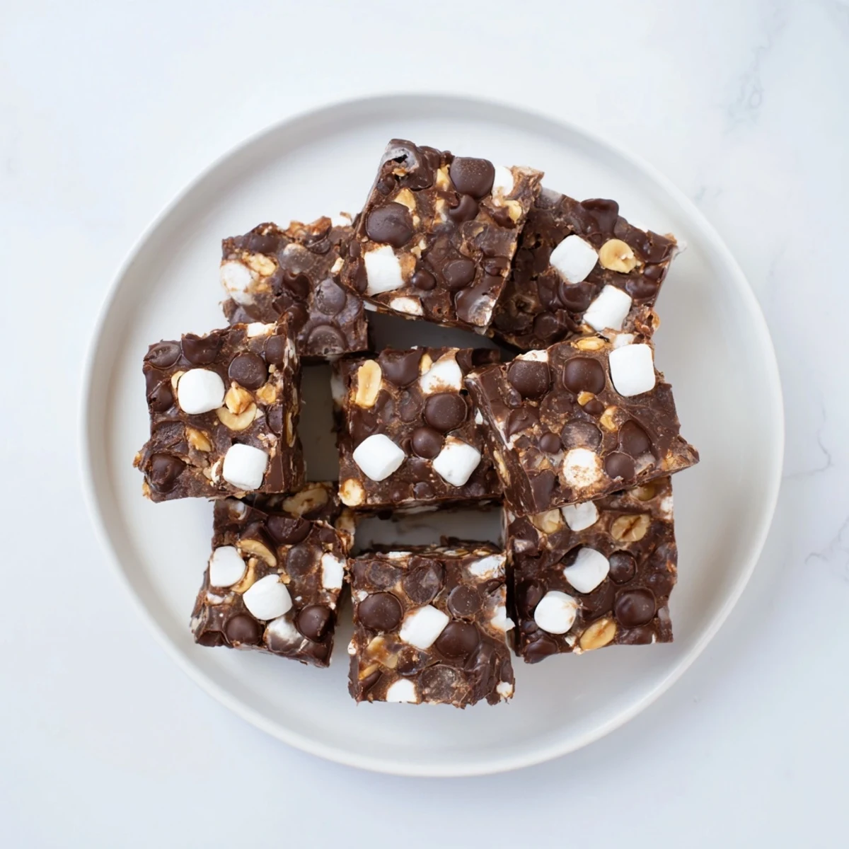 Easy Rocky Road Fudge squares studded with fluffy marshmallows and roasted peanuts on a white plate