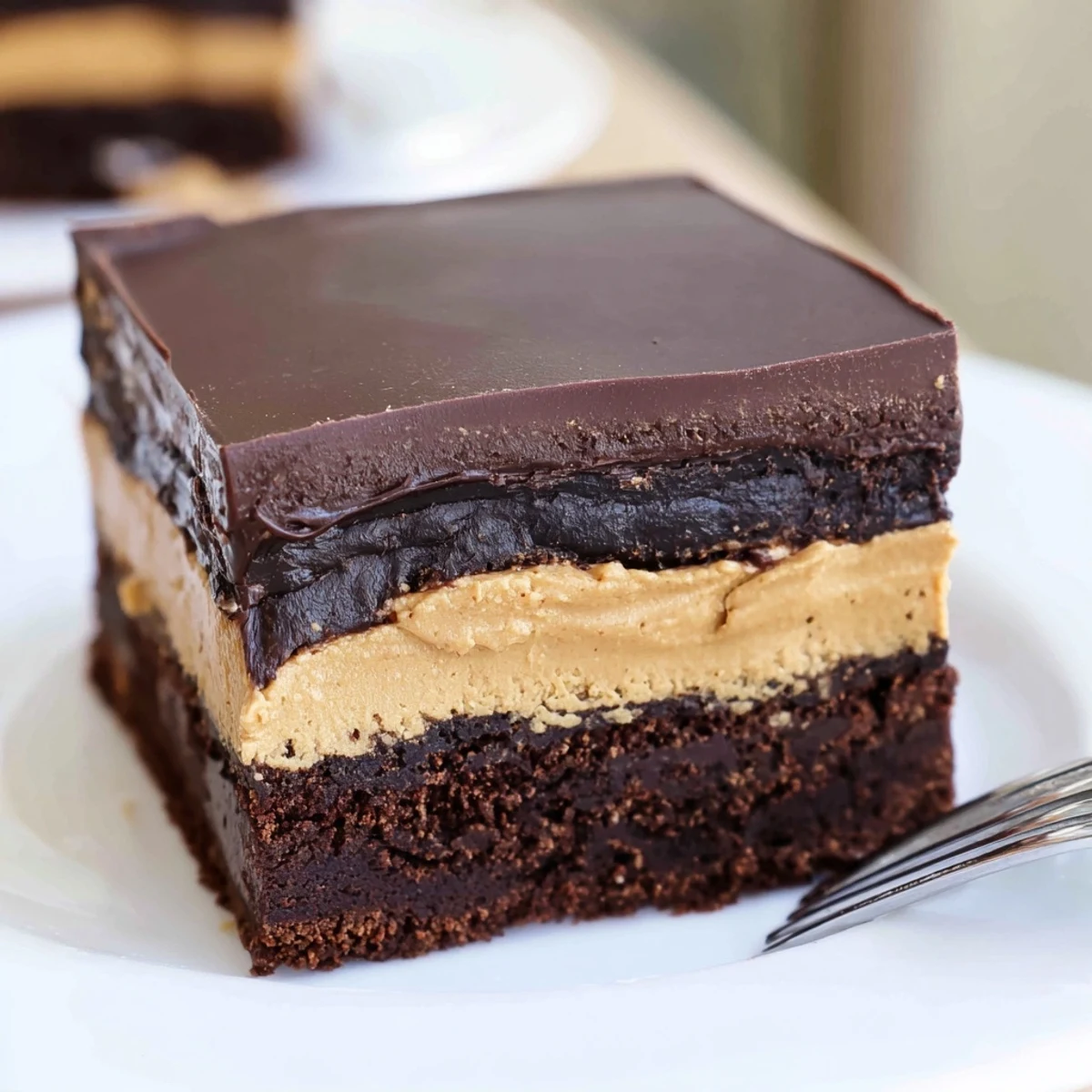 Square slice of layered peanut butter brownies revealing three distinct textured layers of rich chocolate and smooth peanut butter