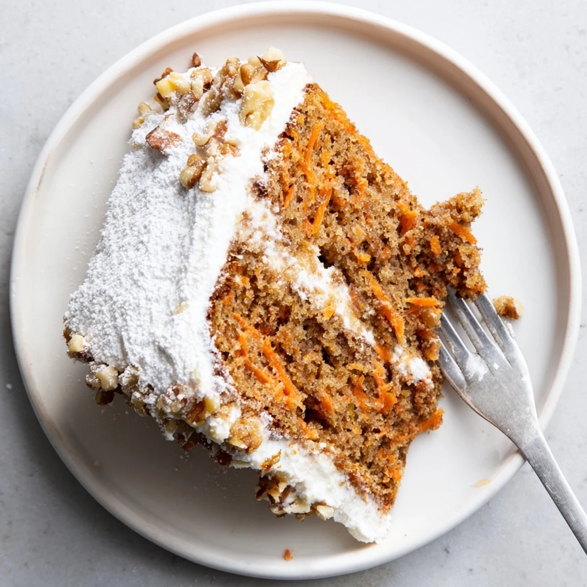 Golden slice of Greek yogurt carrot cake one bowl topped with powdered sugar on a white plate