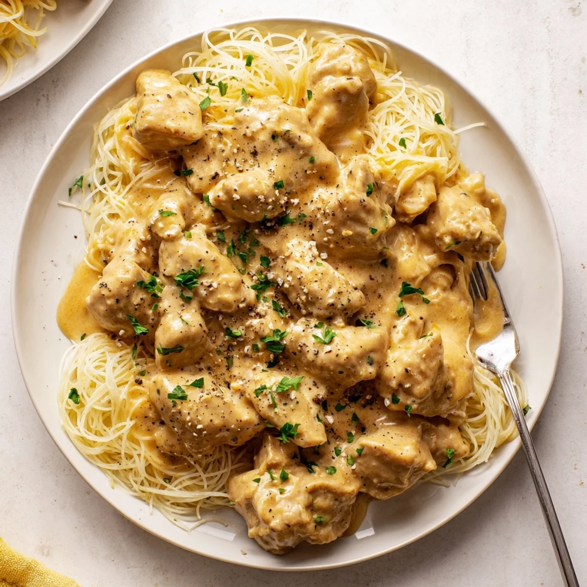 Succulent slow-cooked chicken breasts in rich cream cheese sauce draped over fluffy white pasta noodles