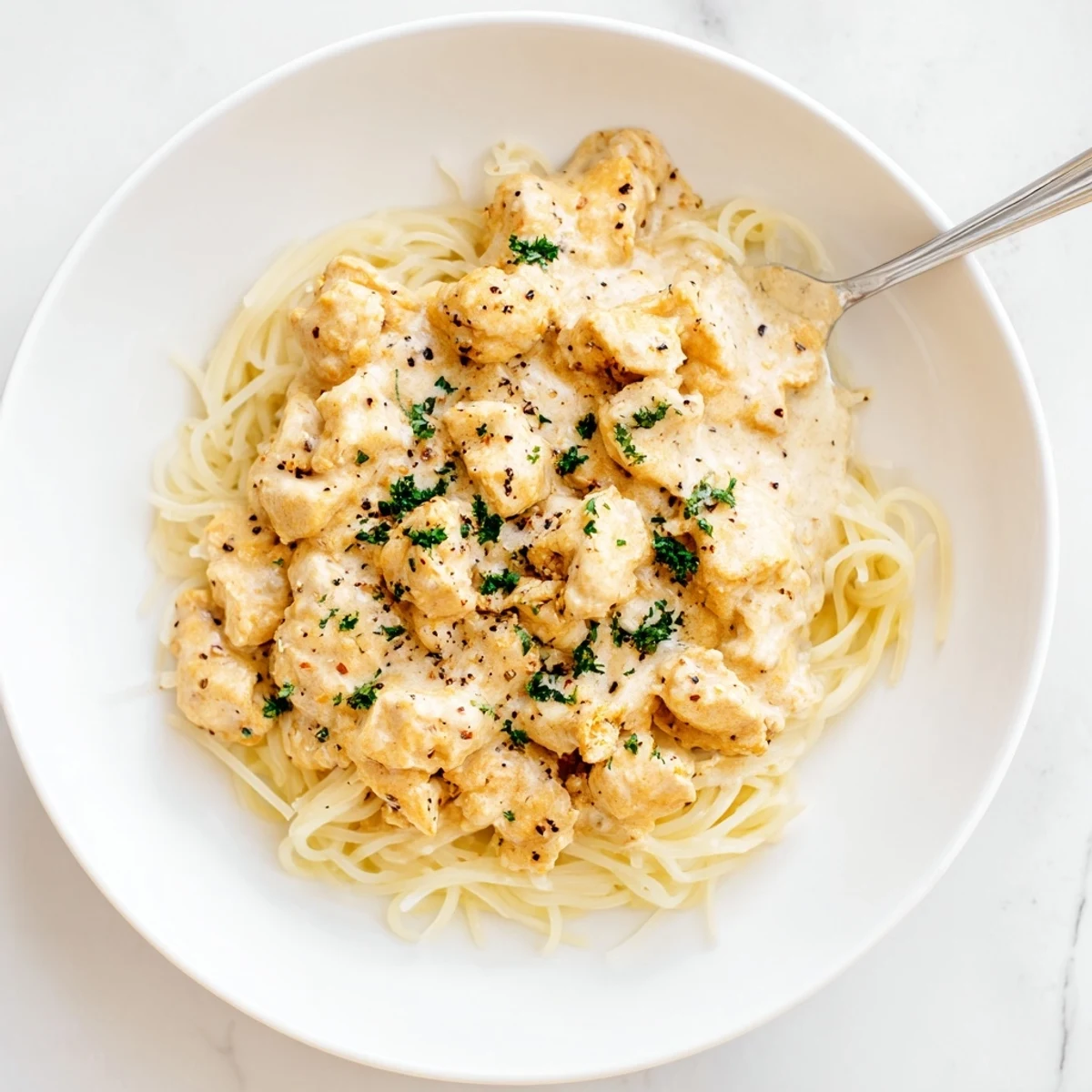 Golden angel hair pasta topped with shredded chicken in velvety Italian cream sauce with parsley garnish