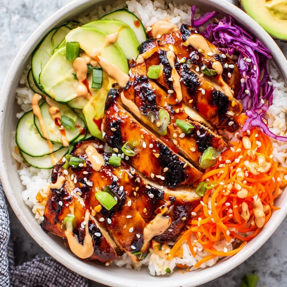 Vibrant Korean BBQ chicken bowl arranged over fluffy jasmine rice topped with avocado slices, shredded veggies and sesame seed garnish