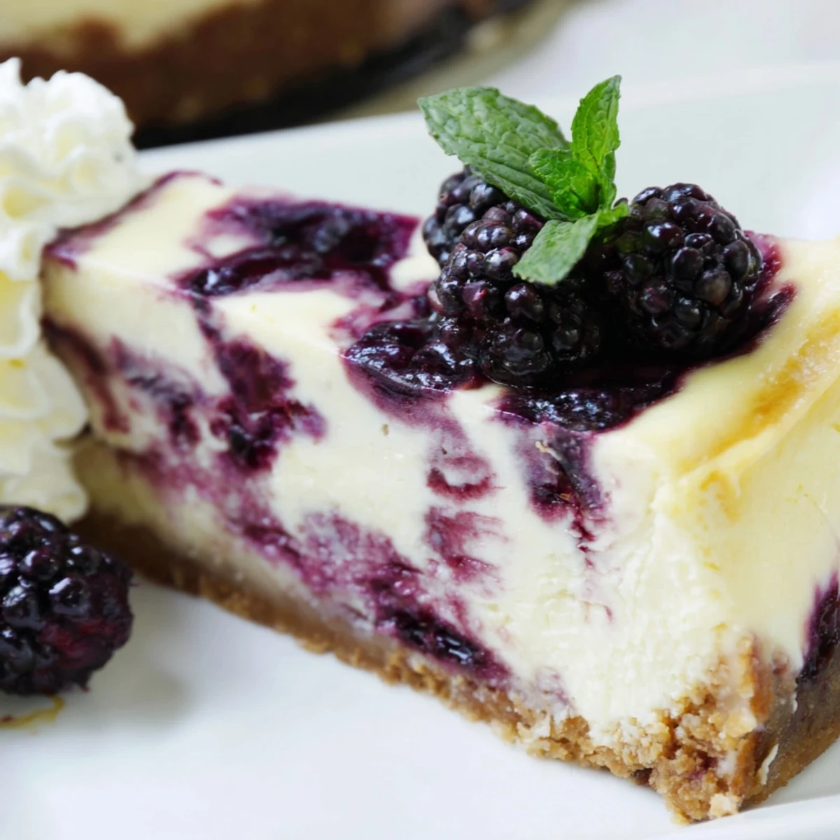 Slice of Blackberry Bliss Cheesecake topped with fresh mint leaves and whipped cream