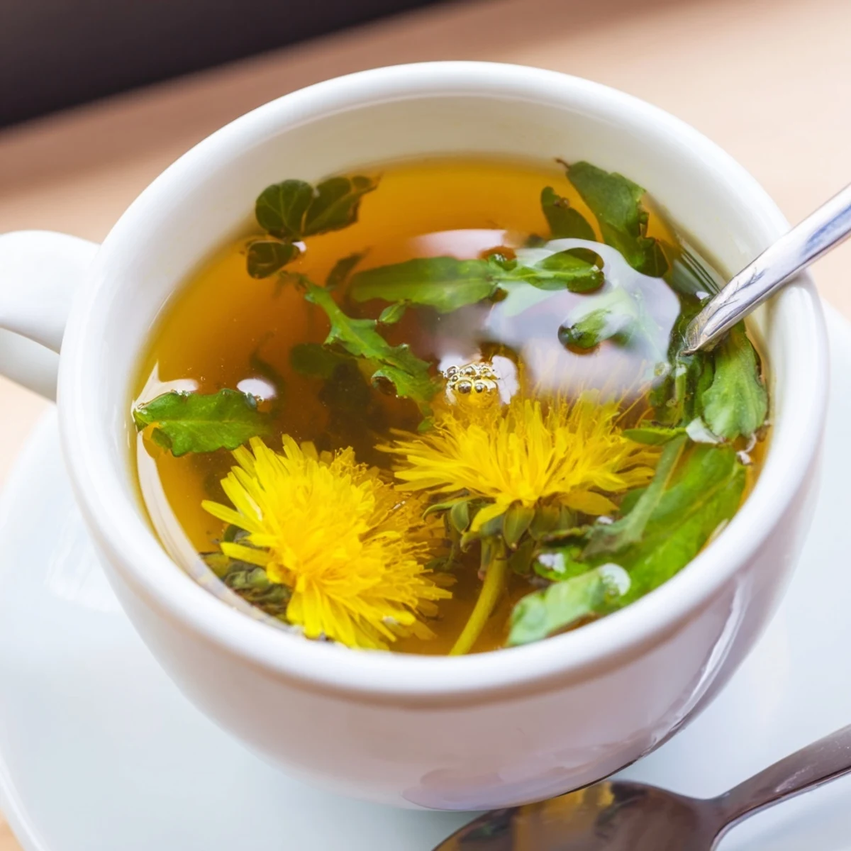 Golden dandelion tea steaming in a white ceramic cup with fresh lemon wedge on wooden table