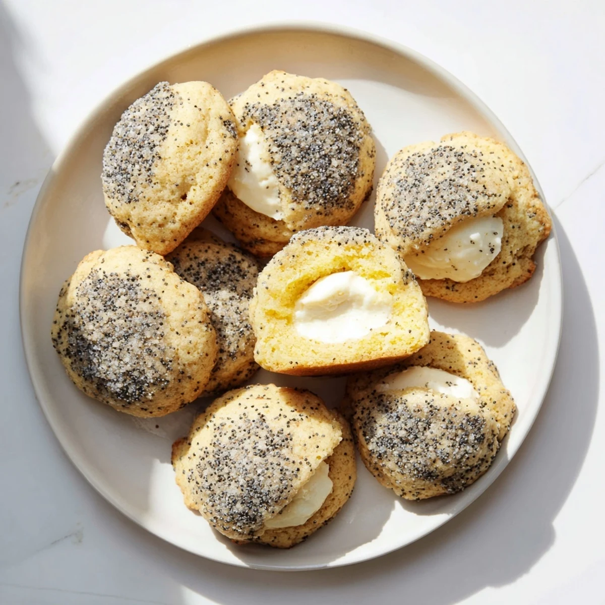 Two bite-sized lemon poppy seed cheesecake cookies with visible cream cheese filling and cracked tops
