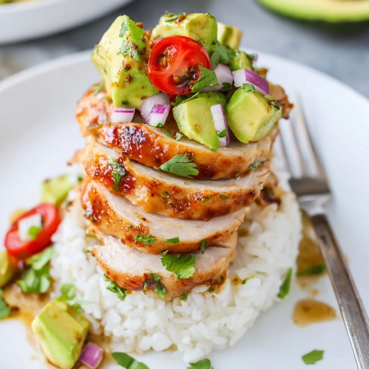 Honey lime chicken avocado rice stack featuring grilled marinated chicken breast stacked over bright green avocado and rice garnished with cherry tomatoes and herbs