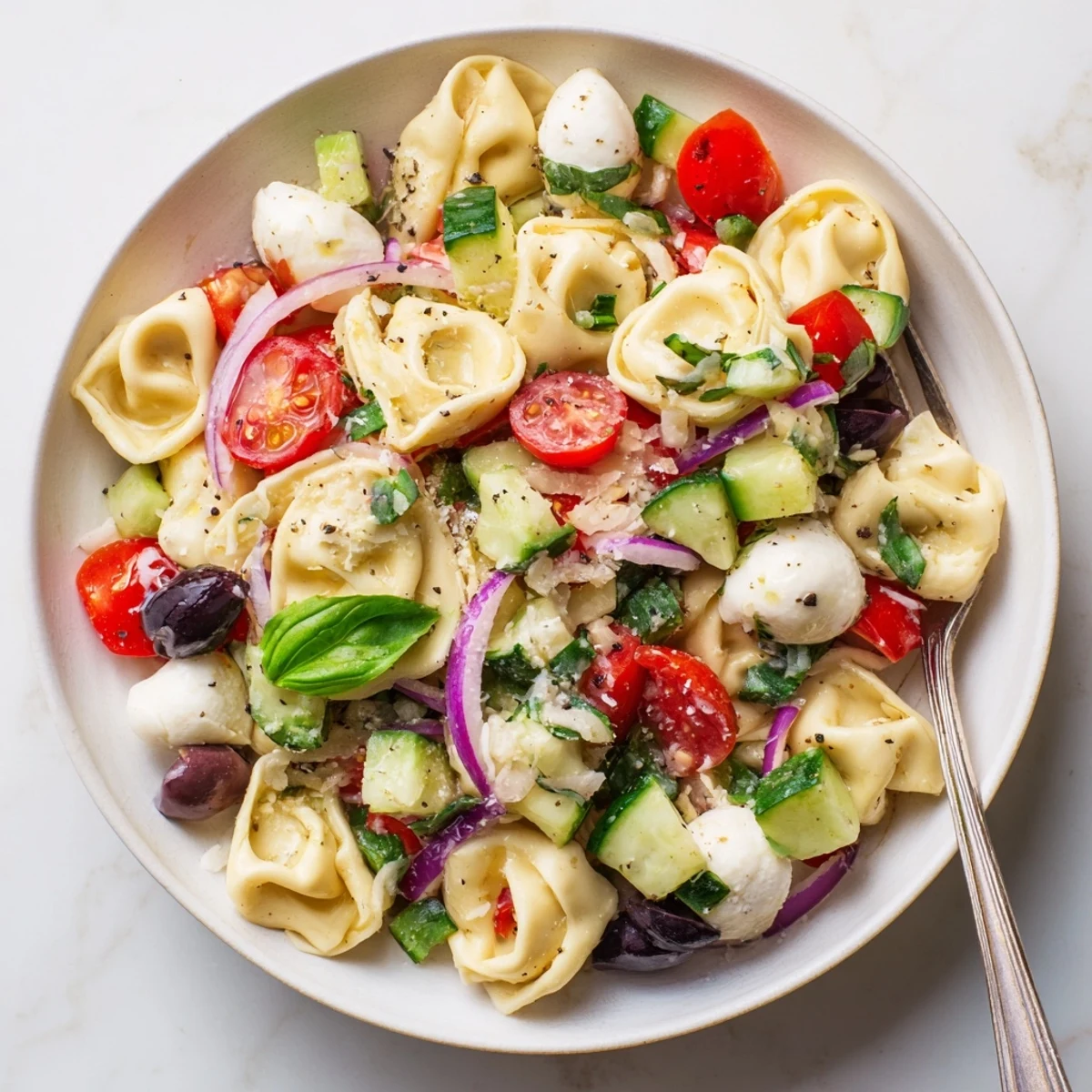 Cheese tortellini salad featuring ripe cherry tomatoes, cucumber, and fresh basil leaves