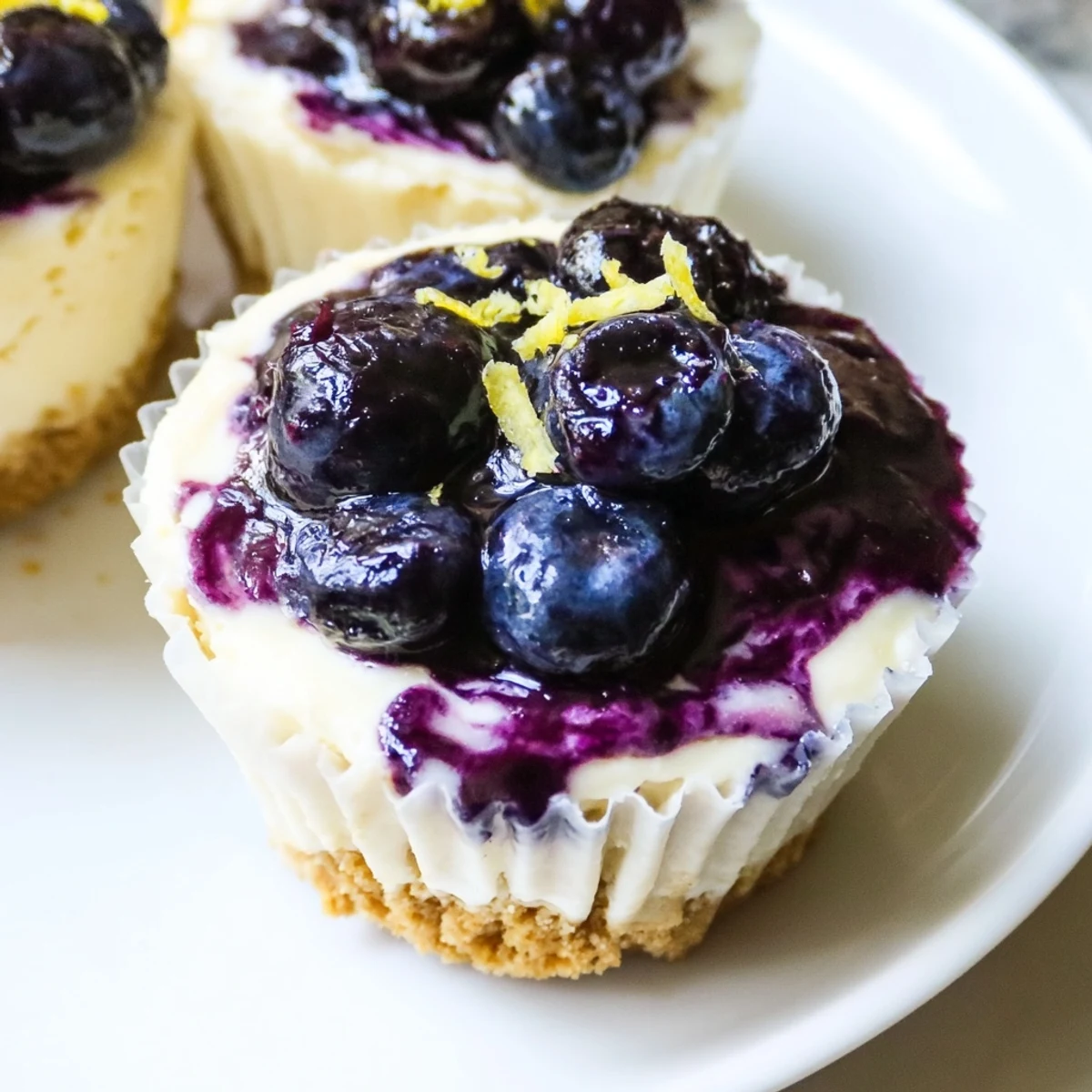 Individual mini lemon blueberry cheesecakes garnished with fresh berries and bright lemon zest