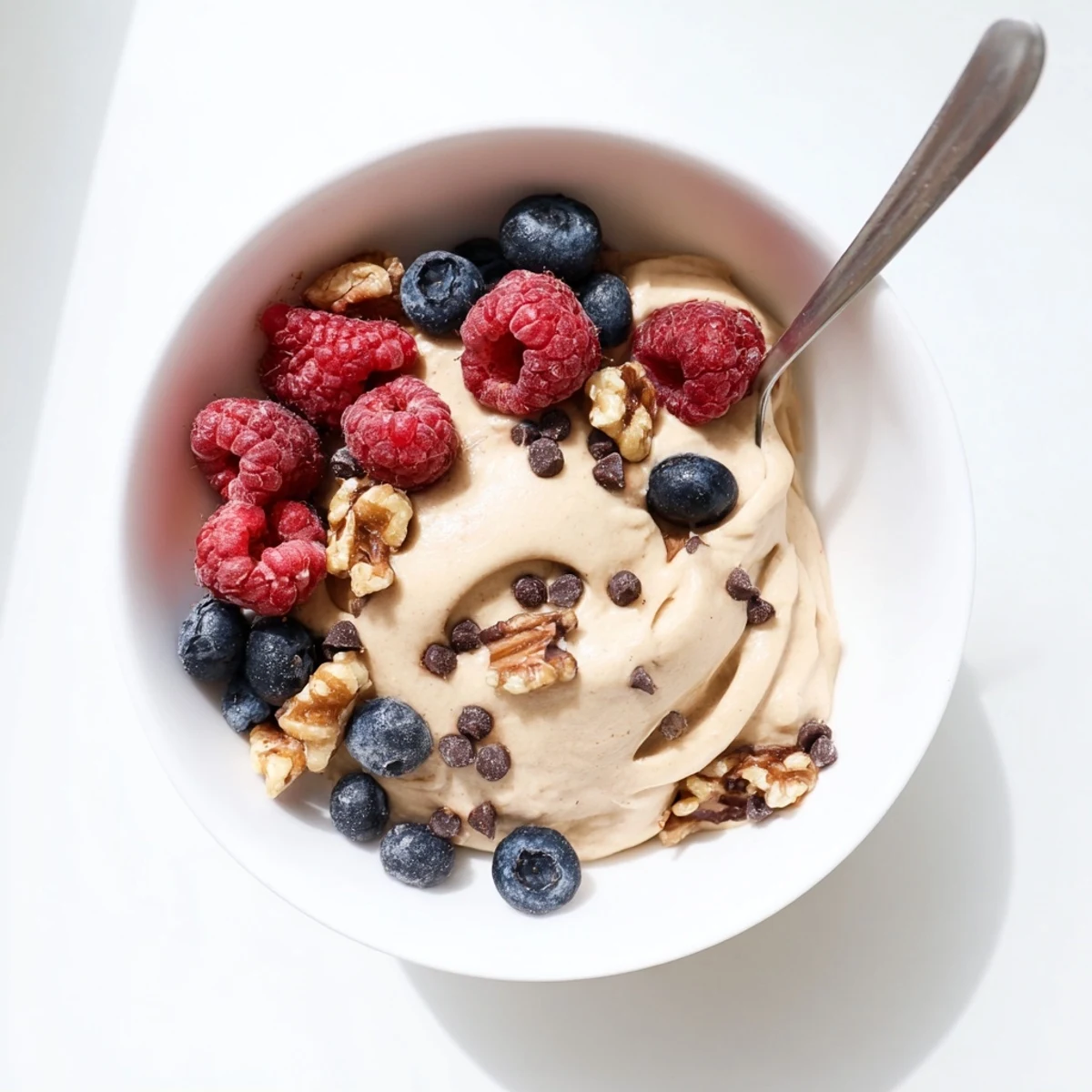 Creamy banana nice cream scooped into a bowl topped with fresh berries and chopped nuts