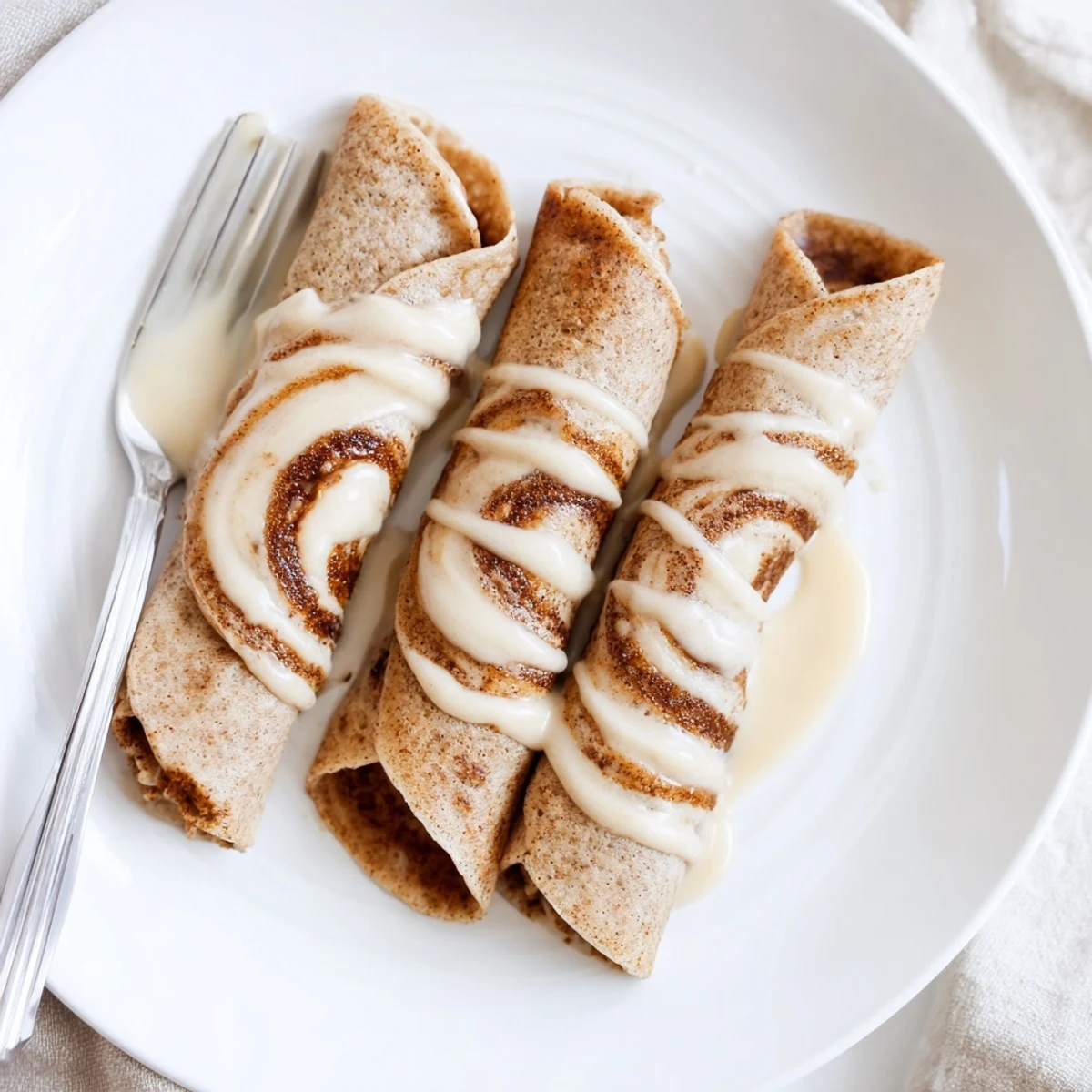 Thin Cinnamon Roll Protein Crepes topped with creamy glaze and a dusting of cinnamon
