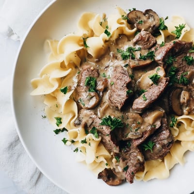 Hearty Beef Stroganoff with Egg Noodles served steaming hot, featuring golden noodles and savory beef in a velvety sour cream sauce.